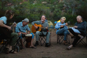 A group of people site in camp chairs and play instruments