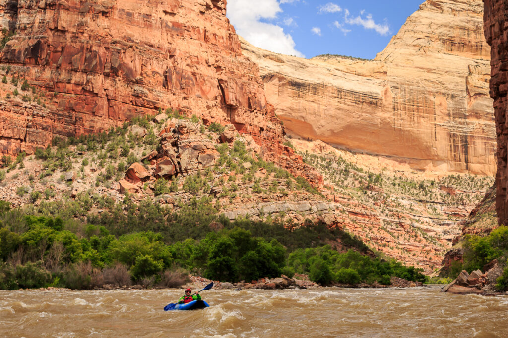 a raft paddles down a scenic secion of the yampa river as the sun rises on the canyon walls
