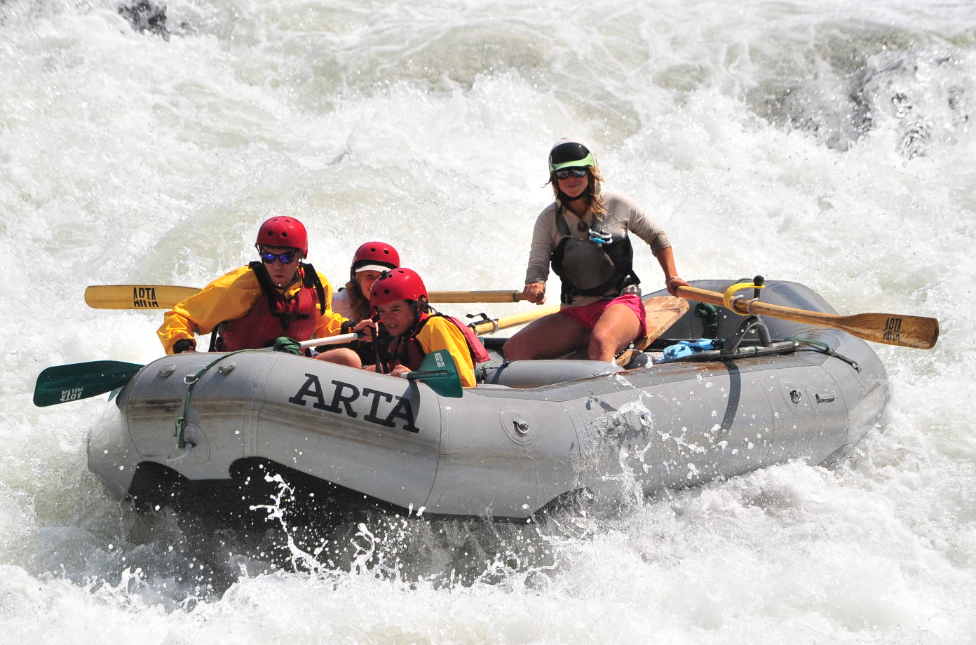 A guide in a grey boat leads three people down the tuolumne river