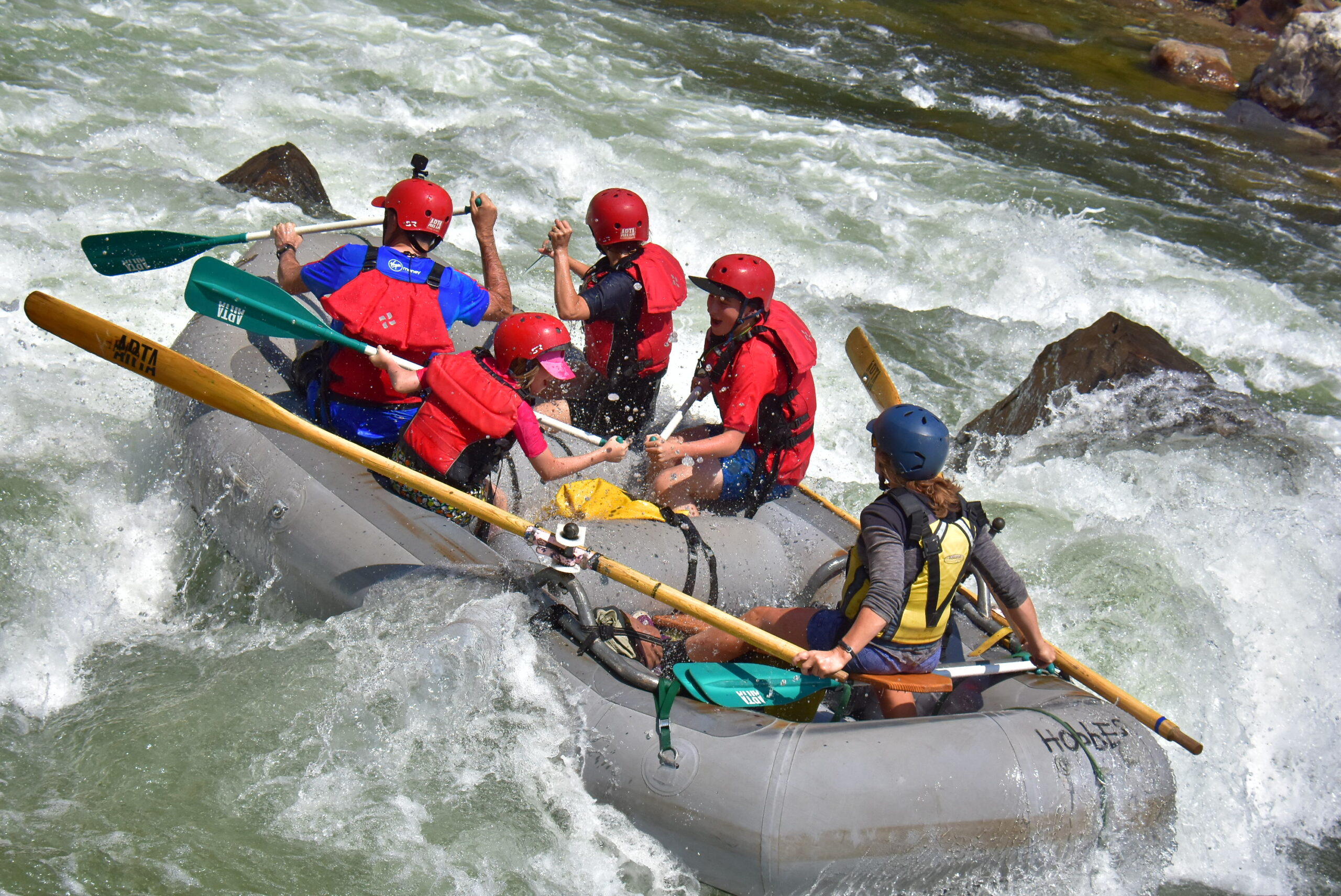 A guide paddles a grey boat through rapids