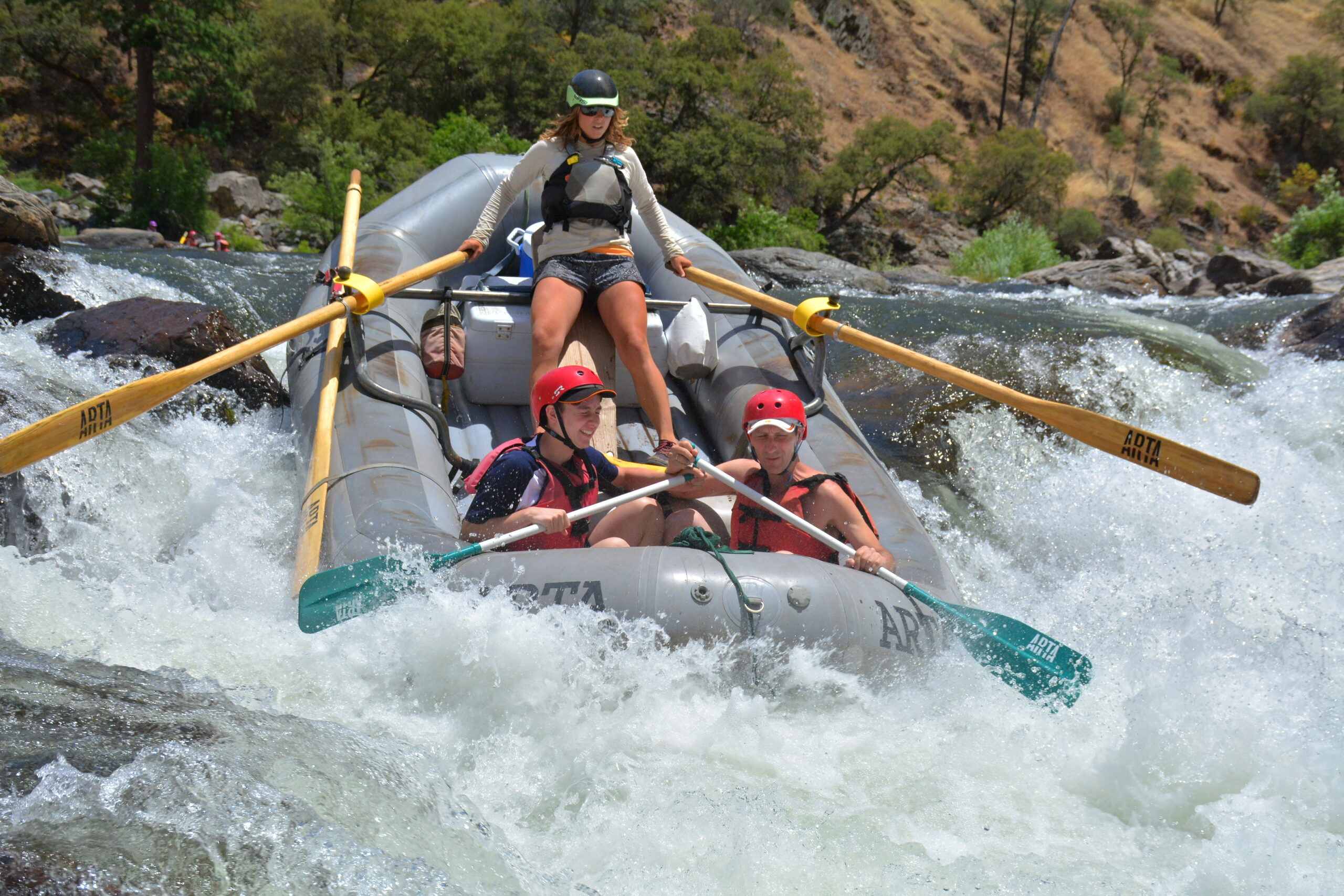 A river guides paddles a boat through a rapid