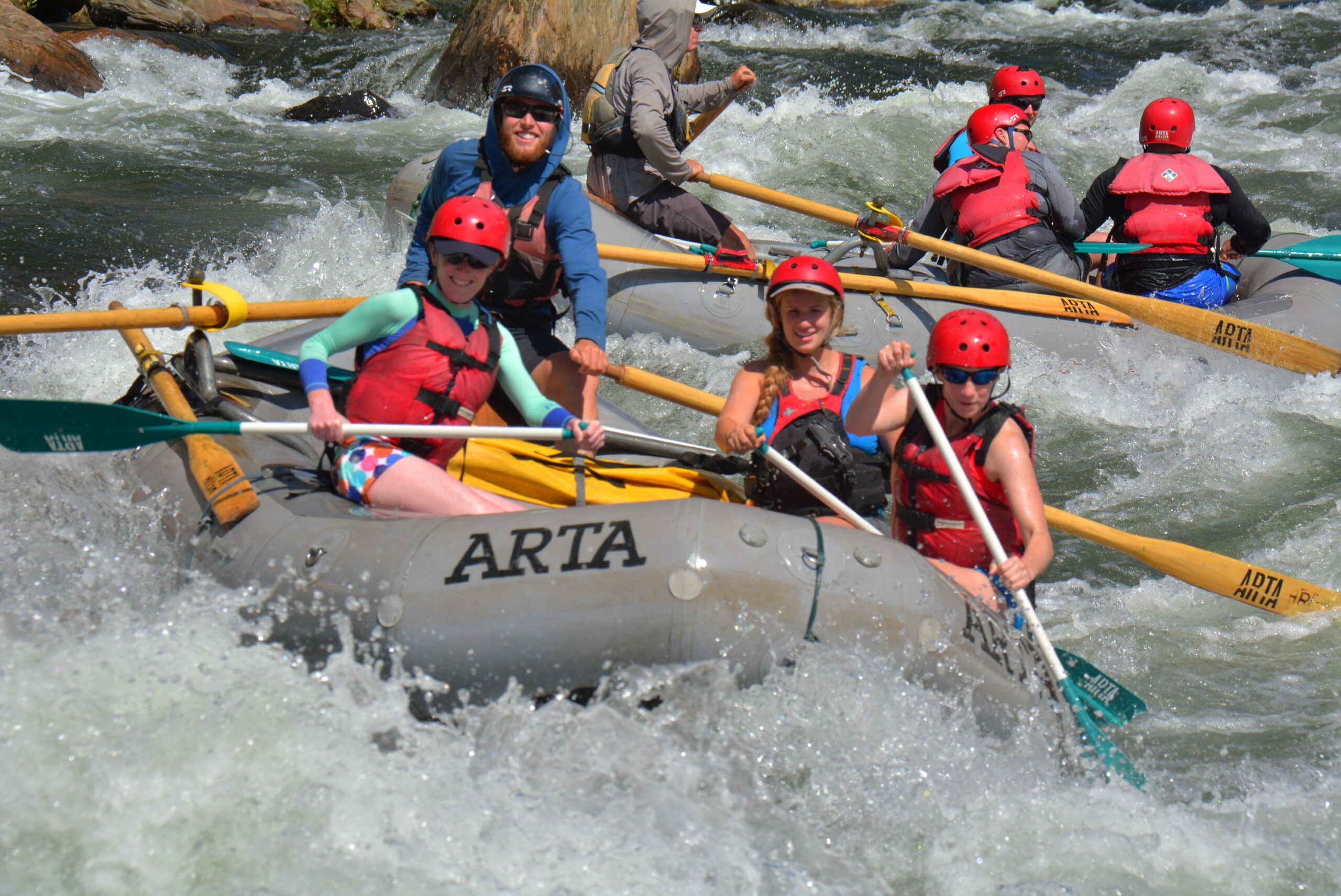 A grey boat with passengers rafts through rapids