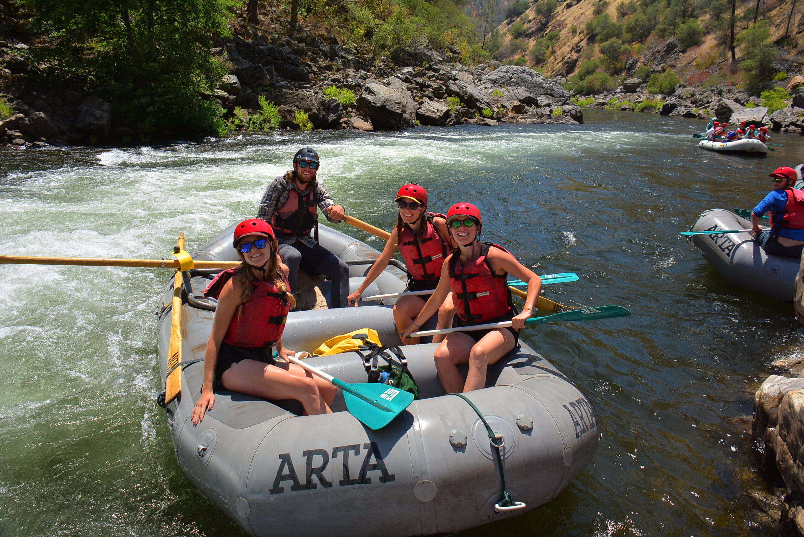 A raft guide on a raft with three passengers