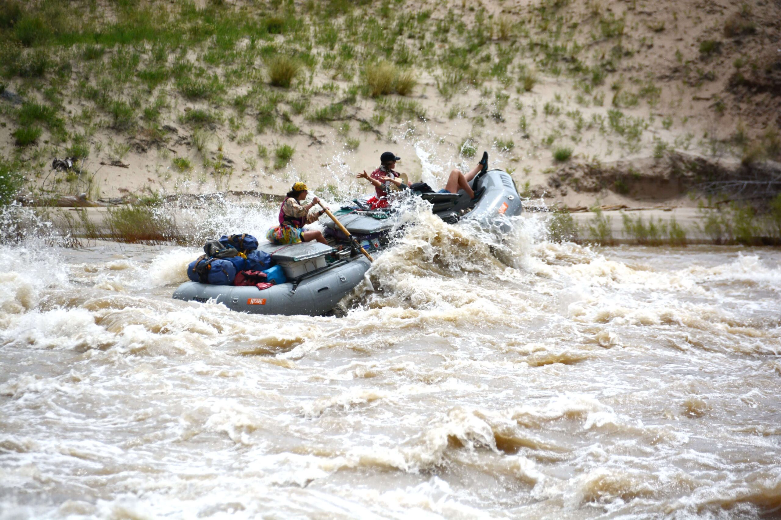 A grey raft with three people paddle through whitewater rapids
